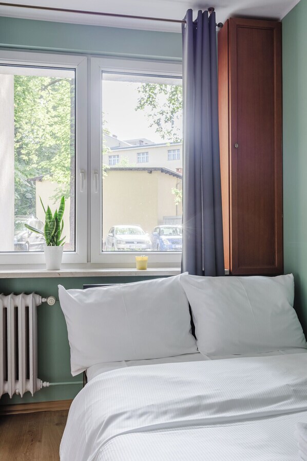 A bedroom with a bed, a window with curtains, a radiator, and a potted plant.