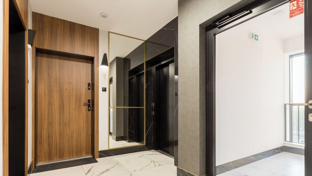 Un couloir moderne avec une porte en bois, un mur miroir et un ascenseur.