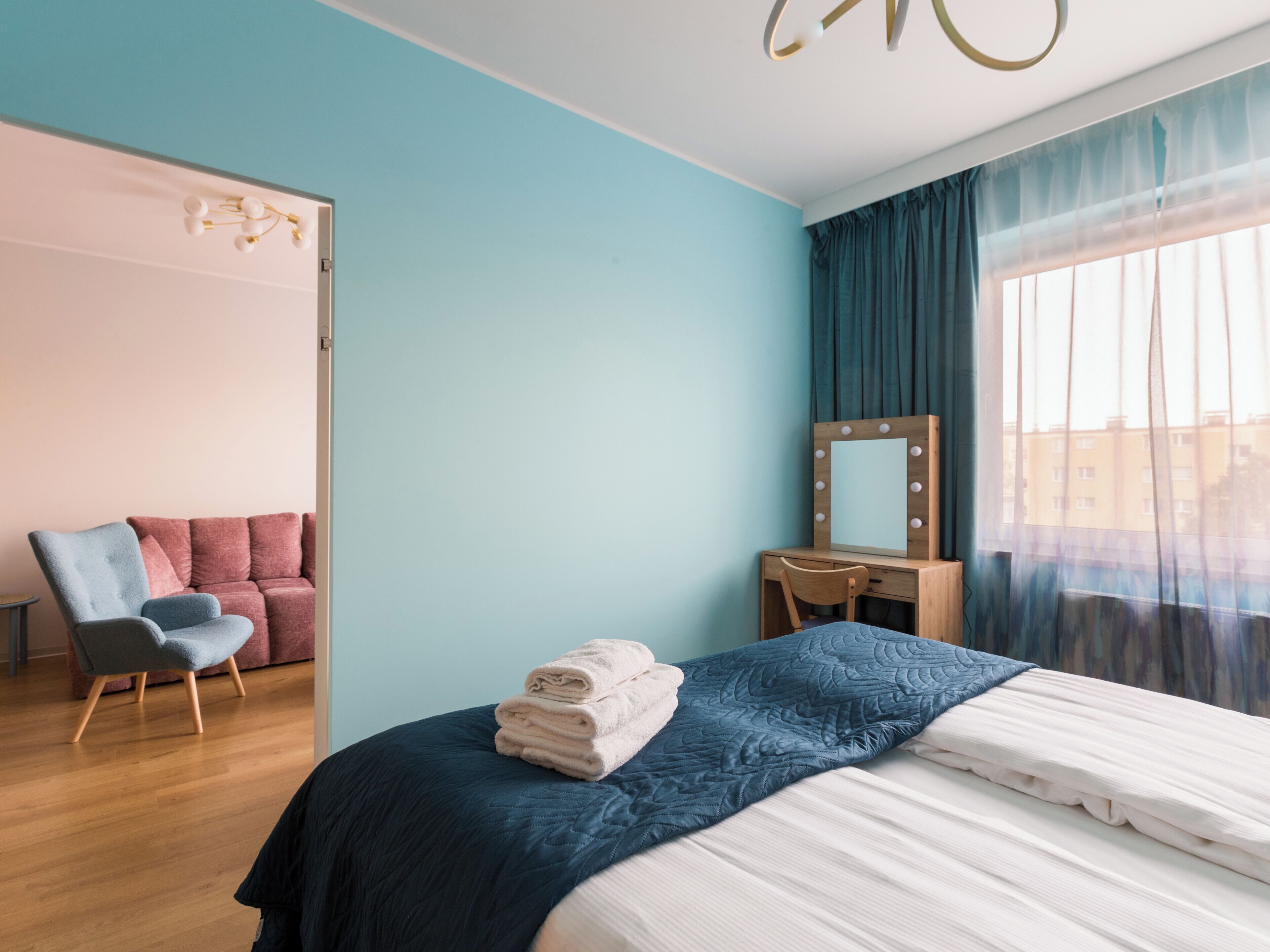 A modern bedroom with a bed, a chair, a vanity with a mirror, and a window with curtains.