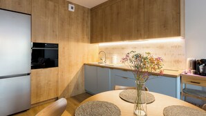 Une cuisine moderne avec des meubles en bois, un four encastré, un réfrigérateur en acier inoxydable, une table de salle à manger ronde avec des sets de table en fibres tressées et un vase rempli de fleurs.