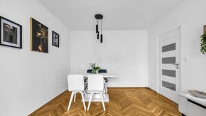 Ein moderner Essbereich mit einem weißen Tisch, zwei weißen Stühlen, einer hängenden Leuchte und einem Holzboden mit Fischgrätmuster.