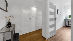Ein Flur mit weißen Türen, einem Schreibtisch mit Blumenvase und Holzboden.