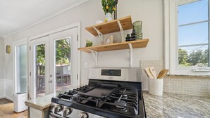 Une cuisine équipée d’une cuisinière à gaz, de rayonnages en bois et d’une fenêtre donnant sur les arbres.