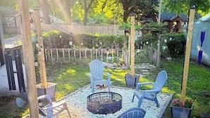 Un jardin avec un foyer, deux fauteuils Adirondack et une clôture en bois.