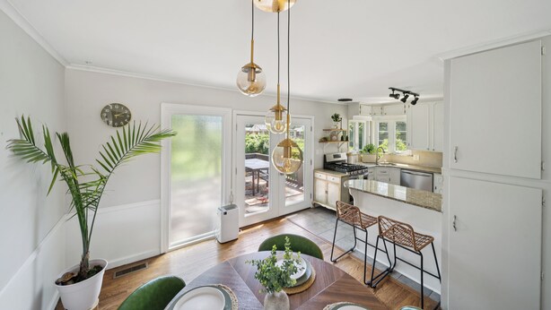 Une cuisine moderne avec des meubles blancs, un coin repas doté d’une table en bois et une grande plante en pot.