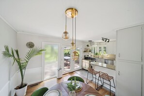 A modern kitchen with white cabinets, a dining area with a wooden table, and a large potted plant. - Earth & Echo-Nature-Inspired - Themed Bedrooms + Firepit + Walk to Brookside (Tulsa)