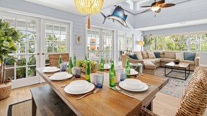 A spacious dining area with a wooden table set for six, surrounded by large windows and a ceiling fan. - Salty Sailfish | Private Pool + Hot Tub + Siesta Key (Sarasota)