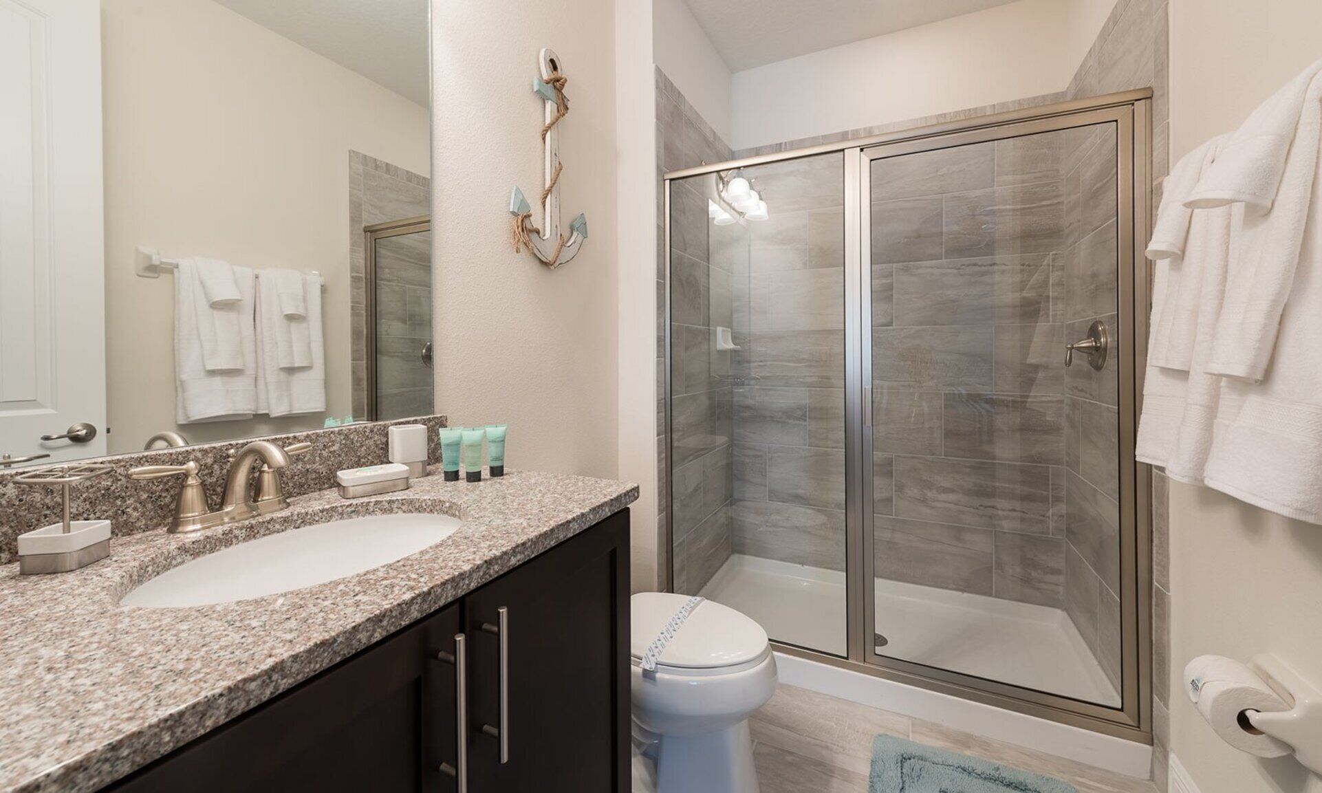 A bathroom with a granite countertop, a double sink, a toilet, a shower with glass doors, and a towel rack with towels.