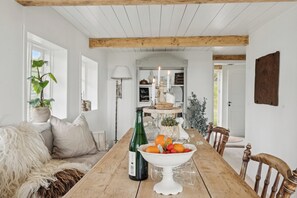 Ein Holztisch mit Obstschale und Weinflasche, ein weißes Sofa mit Felldecke und eine Pflanze im Blumentopf.