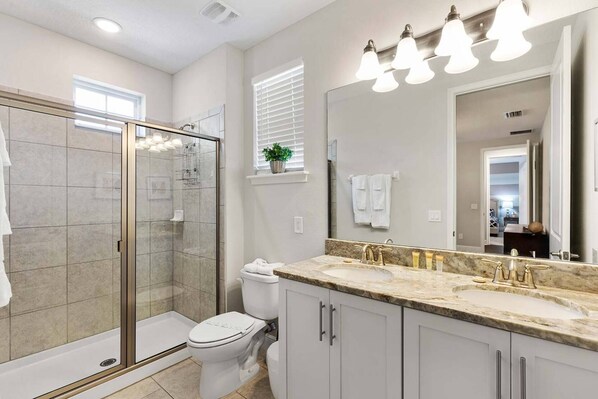A modern bathroom with a glass-enclosed shower, a toilet, a sink with a marble countertop, and a large mirror.