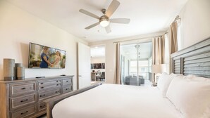 Une chambre d’hôtel dotée d’un grand lit, d’un ventilateur de plafond, d’un téléviseur à écran plat fixé au mur, et offrant une vue sur le balcon et l’espace extérieur aménagé en coin salon.