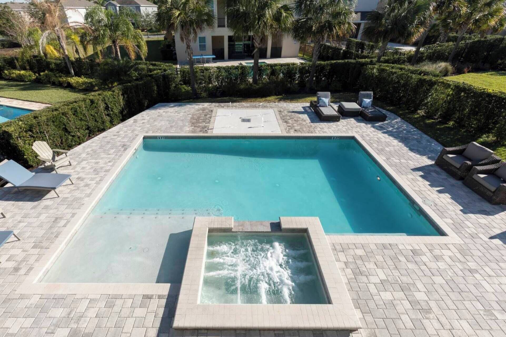 A rectangular swimming pool with a built-in jacuzzi, surrounded by a brick deck and lounge chairs.