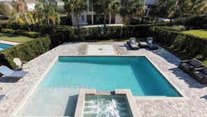 Une piscine rectangulaire dotée d’un jacuzzi intégré, entourée d’une terrasse en briques et de chaises longues.