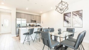 Een moderne keuken met een centraal kookeiland, roestvrijstalen apparatuur en een eethoek met een glazen tafel en zwarte stoelen.