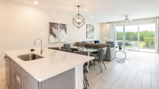 Een moderne keuken met een centraal eiland, een eethoek met een glazen tafel, en een zithoek met een bank en stoelen.