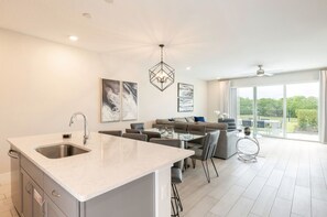 Una cocina moderna con una isla central, un comedor con una mesa de vidrio y una sala de estar con sofá y sillones.