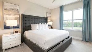 Een slaapkamer met een groot bed, een nachtkastje, een lamp, een plafondventilator en een raam met gordijnen.