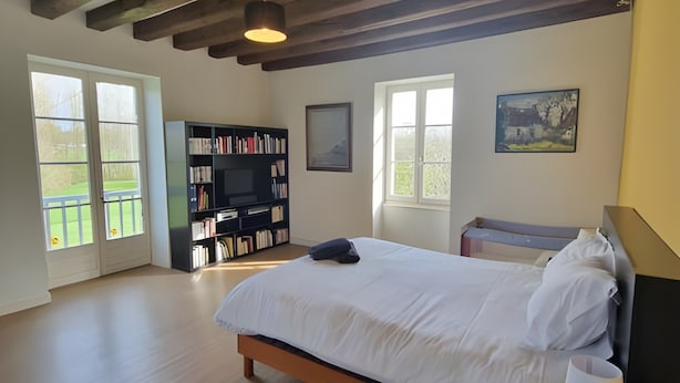 A bedroom with a wooden bed, a bedside table with a lamp, a bookshelf, and a window with a view of greenery. - Heritage Hideaway With Garden & Charm (Thorée-les-Pins)