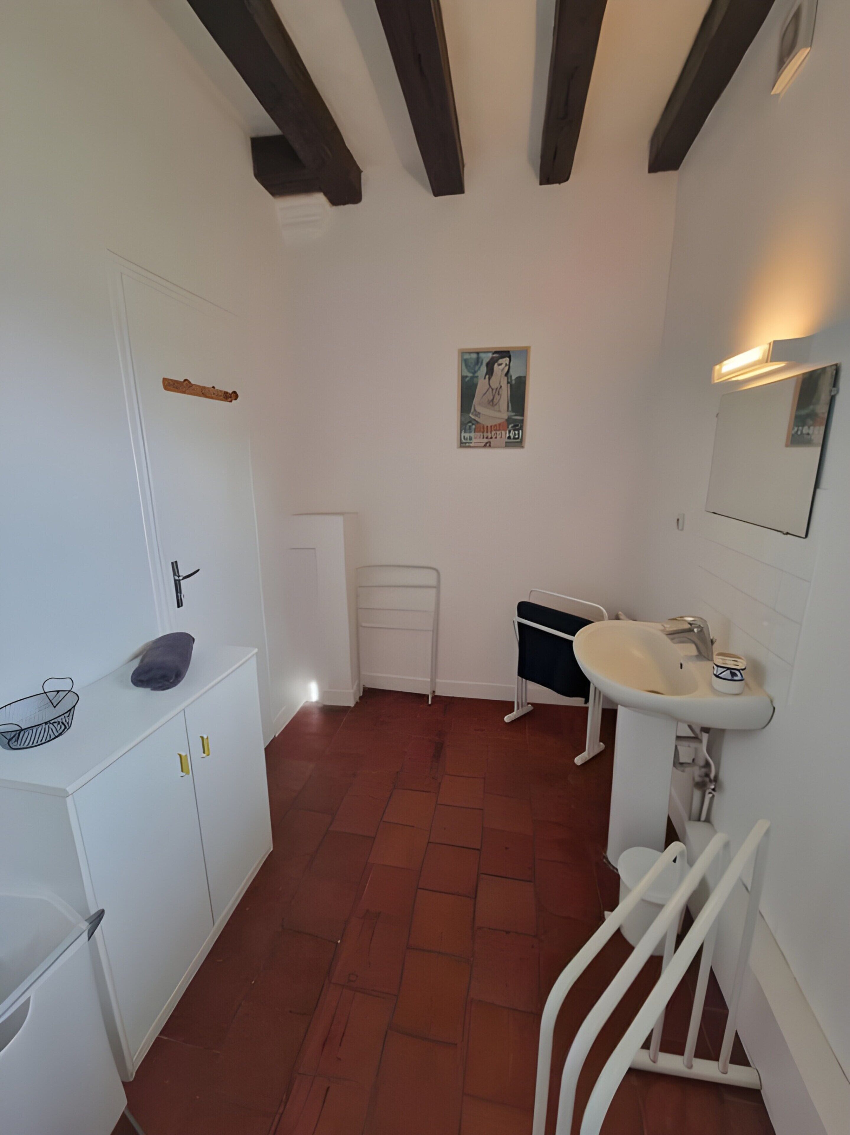 Une petite salle de bain compacte, avec un lavabo blanc, un miroir, un porte-serviettes et un petit radiateur.