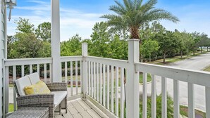 A porch with a white railing, wicker furniture, and a view of a street lined with trees. - Embrace Luxury: Your Perfect Escape, Orlando Villa 1000 (Kissimmee)