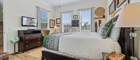 A bedroom with a bed, a ceiling fan, a TV, and a dresser.