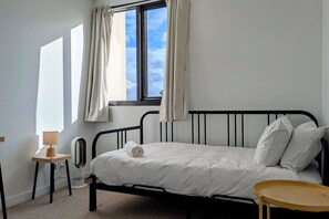 A bedroom with a single bed, a bedside table, a lamp, and a window with curtains. - Townhouse with 2.5 bathrooms and double garage (Burwood)