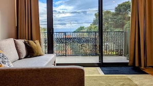 Ett vardagsrum med en soffa, utsikt över en balkong med ett metallstaket och ett stort fönster.
