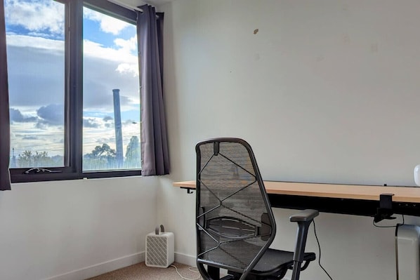 A room with a window, a chair, a desk, and a heater.