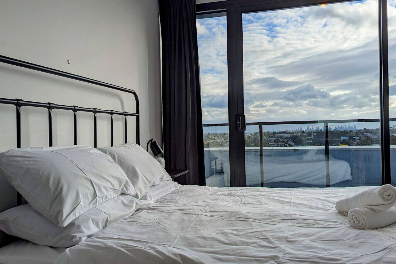 A hotel room with a bed, a window with a city view, and a balcony.