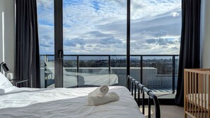 Ett hotellrum med en säng, en spjälsäng i trä och en balkong med utsikt över staden.