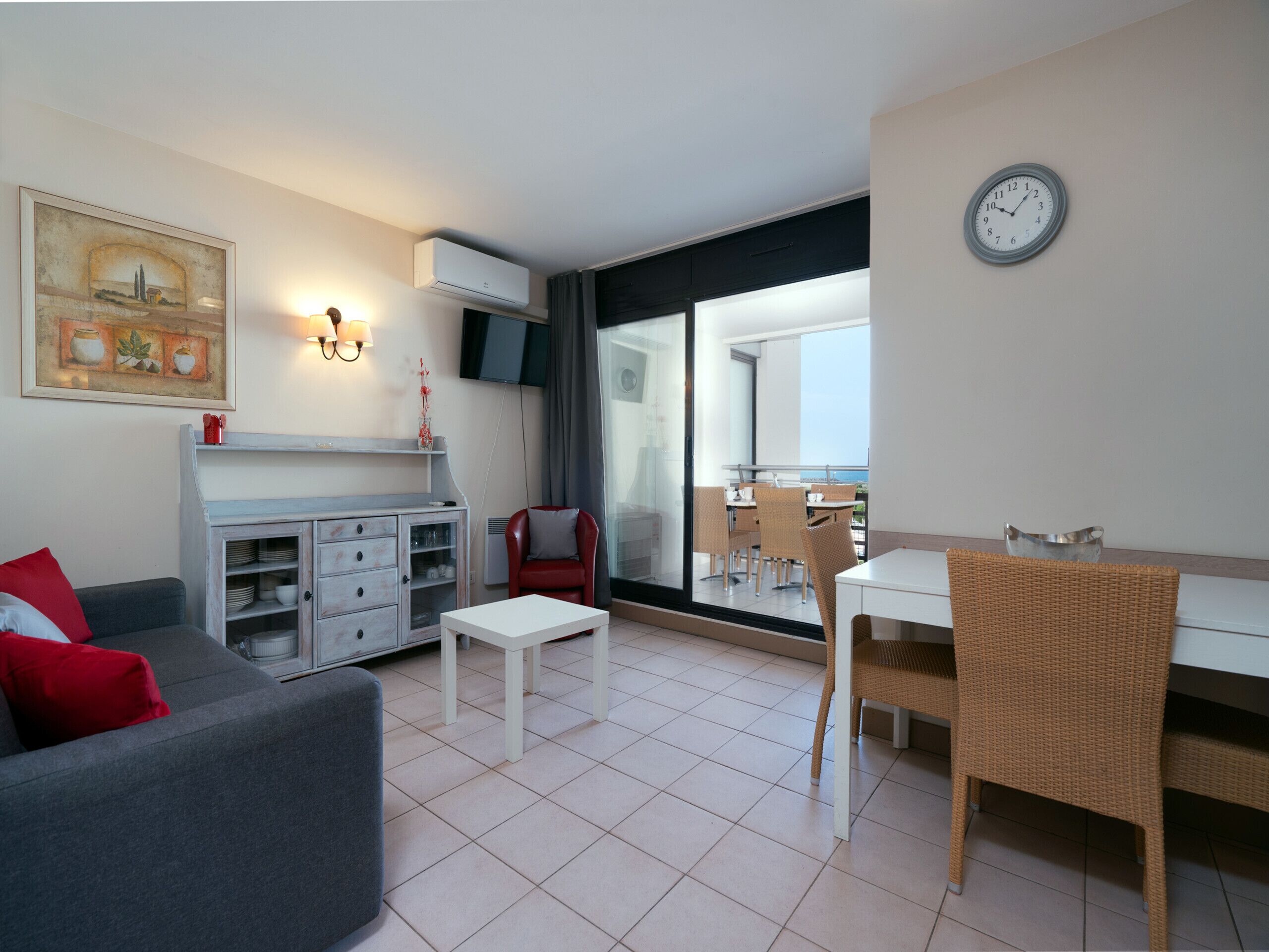 A modern living room with a grey sofa, a white coffee table, and a dining area with wicker chairs and a white table.