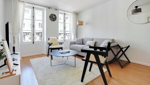 A modern living room with a grey sofa, a round coffee table, a black chair, a white rug, and a TV on a stand.