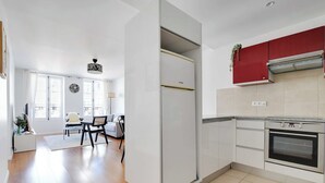 A modern kitchen with white cabinets, a red upper cabinet, a built-in oven, and a dining area with a white chair and table.