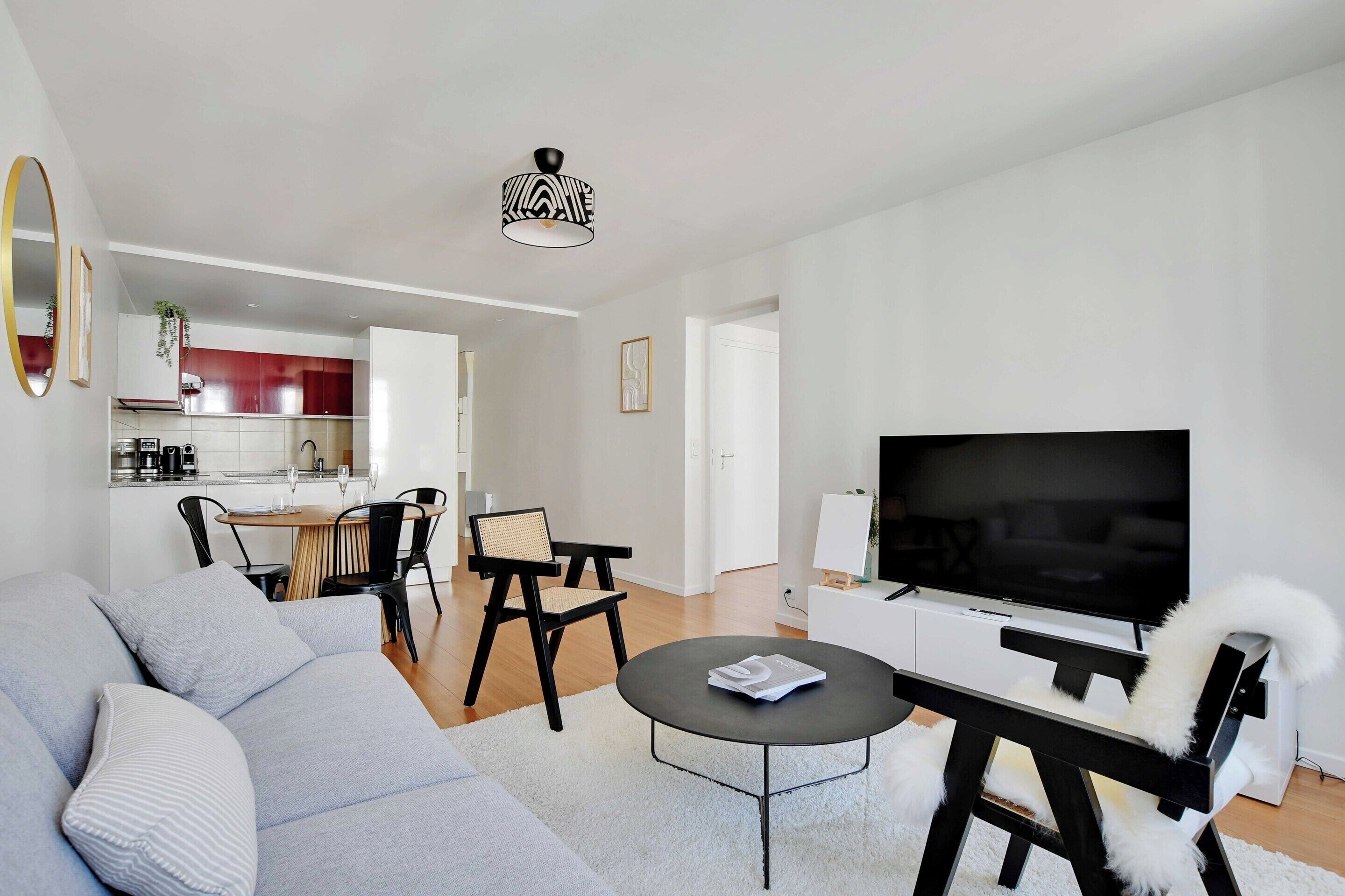 A modern living room with a grey sofa, black chairs, a round coffee table, and a flat-screen TV.