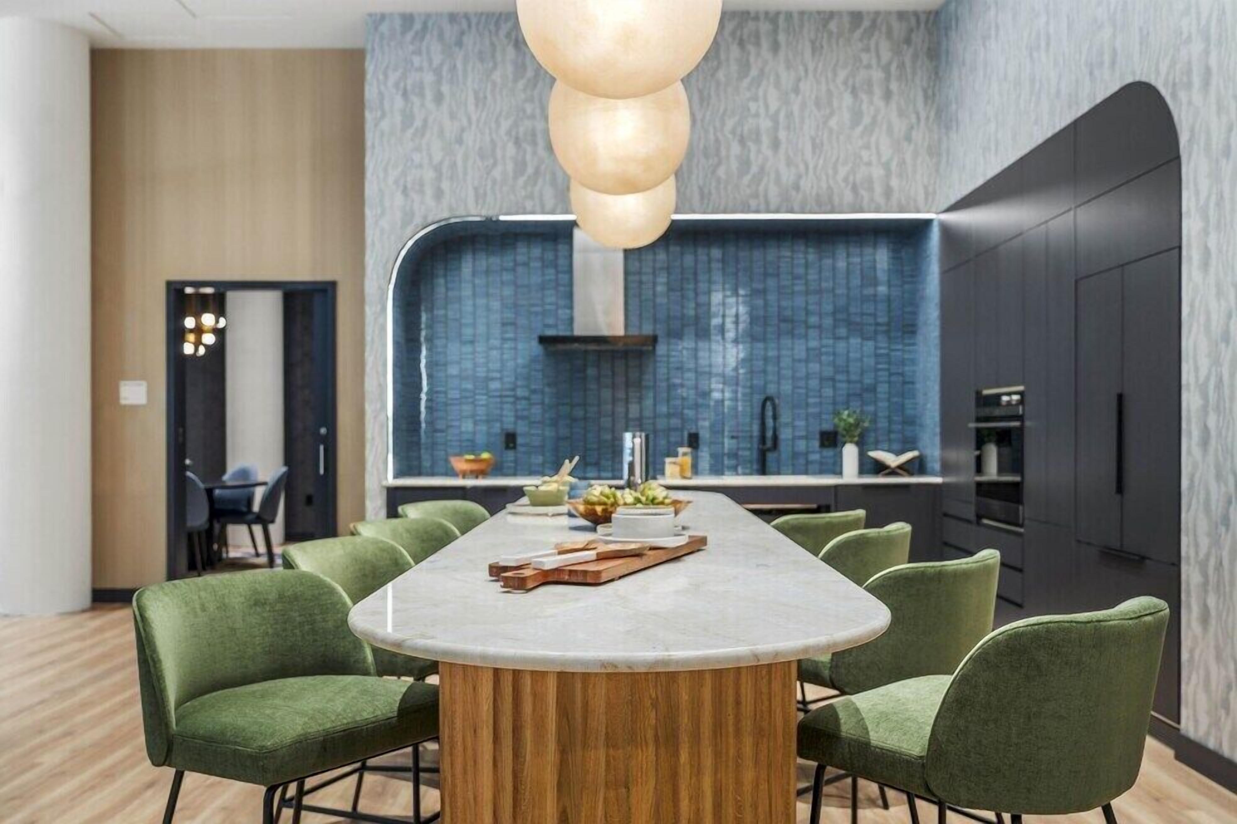 A modern kitchen with a blue backsplash, a central island with chairs, and a wooden ceiling light fixture.