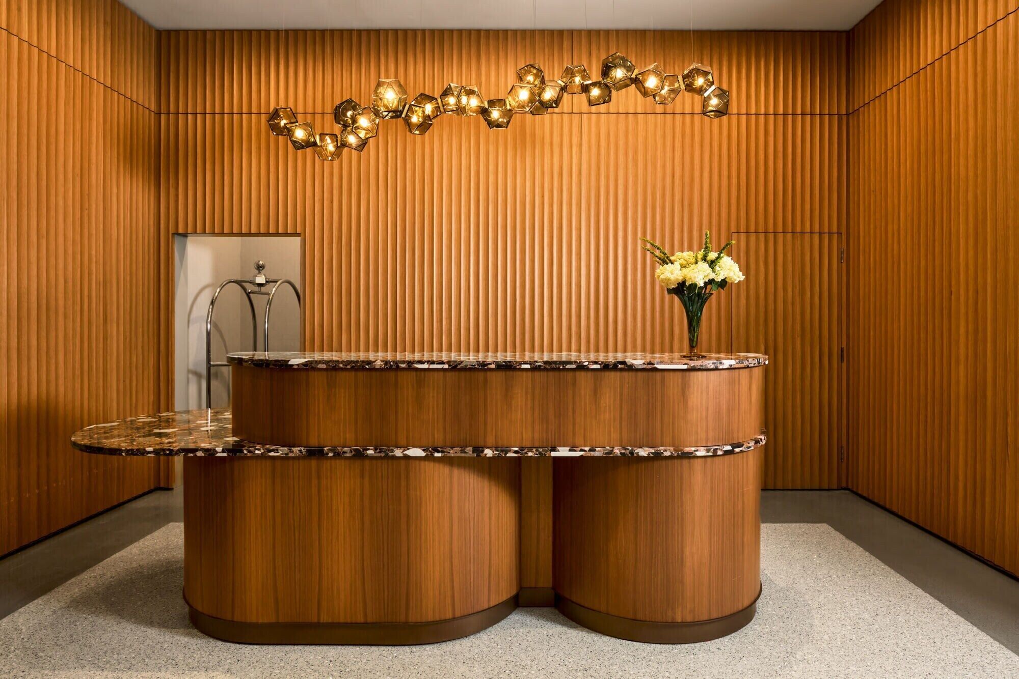 A reception desk with a marble top, a vase with yellow flowers, and a geometric light fixture above.