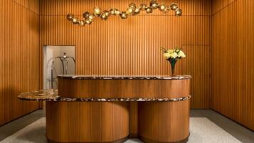 A reception desk with a marble top, a vase with yellow flowers, and a geometric light fixture above.