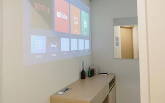 A projection of streaming services on a wall in a room with a wooden desk, a bottle, and a remote control.