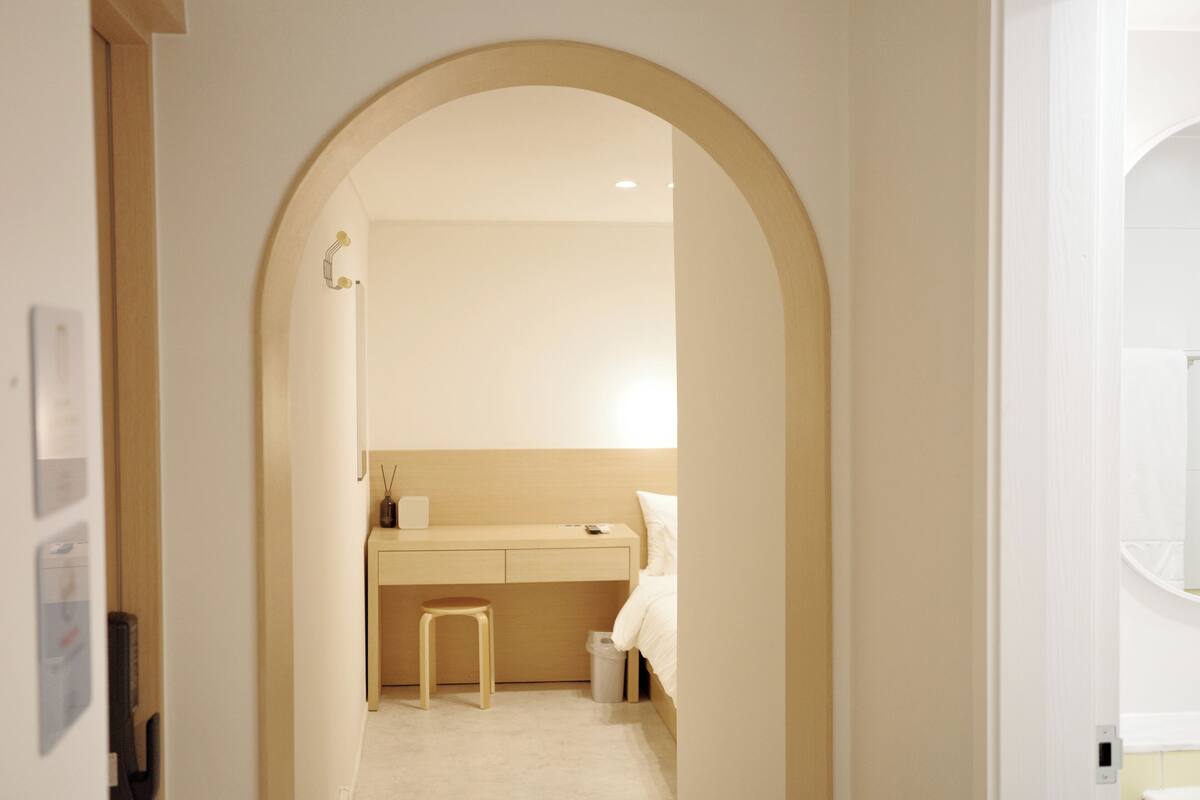 Un dormitorio con estructura de cama de madera, una mesita de noche y un taburete pequeño.