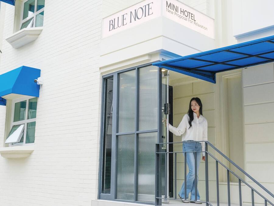 A woman exiting a modern building labeled "BLUE NOTE MINI HOTEL."