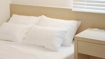 A bed with white bedding and pillows, a wooden headboard, and a bedside table with a power outlet.