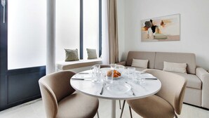Uma área de jantar moderna com uma mesa redonda posta para quatro pessoas, um sofá e uma janela com cortinas.