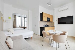 A modern hotel room with a bed, a sofa, a dining area with chairs, a kitchen with a microwave, and a TV mounted on the wall. - Studio Moderne - AC- 4P- Champ-de-mars (Paris)