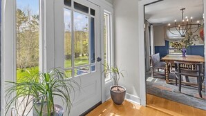 A room with a large window, a potted plant, and a dining area with a chandelier.