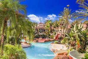 Ein Resort mit einem zentral gelegenen Pool, Palmen und einem Gebäude mit rotem Dach.
