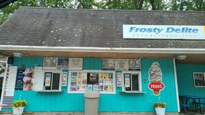 Un magasin de glaces aux couleurs turquoise appelé Frosty Delite, avec un panneau affichant le menu et une pancarte indiquant qu’il est fermé.