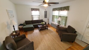Un salon comprenant un canapé, deux fauteuils, une table basse, une lampe sur pied, un radiateur et un ventilateur de plafond.
