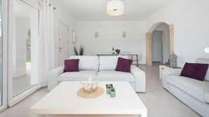 A modern living room with a white sofa, a coffee table, and a glass door leading outside.