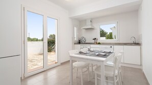A modern kitchen with white cabinetry, a dining table with chairs, and a large window offering a view of the outdoors.