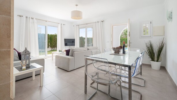 A modern living room with a glass dining table, clear chairs, a sofa, and a TV.